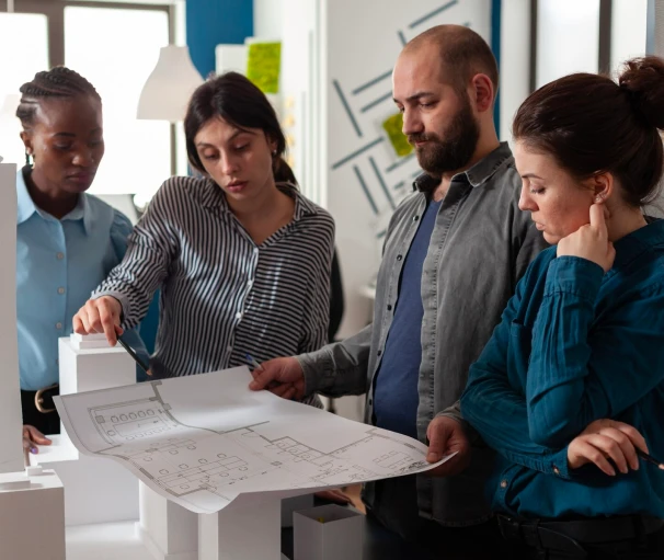 Four professionals examining architectural blueprints in a modern office, engaged in discussion and planning.