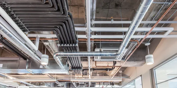 Close-up of exposed pipes and ductwork in a building ceiling.